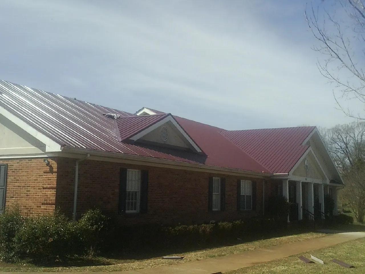 Red metal roof with gabled entries on a long brick building, from a Hail Damage Roof Repair job in Buffalo