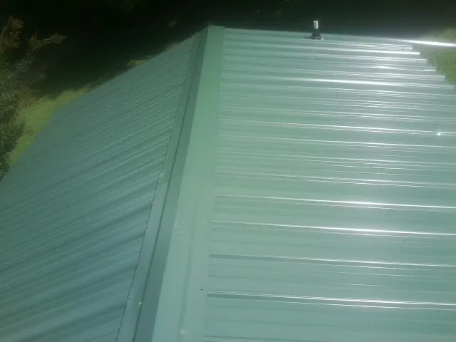New green metal panels meeting at the ridge of a roof — Flat Roof Repair work by our crew in Buffalo